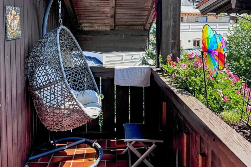 Gefliester Balkon der Ferienwohnung Chiemgauzeit mit einem gemütlichen Hängesessel aus Rattan und ausreichend Sitzmöglichkeiten zum Entspannen.