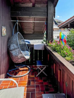 Gefliester Balkon der Ferienwohnung Chiemgauzeit mit einem gemütlichen Hängesessel aus Rattan und ausreichend Sitzmöglichkeiten zum Entspannen.